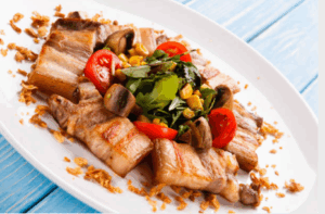 구운 삼겹살과 함께 방울토마토, 버섯, 옥수수, 샐러드 채소가 곁들여져 건강한 식단 느낌을 주는 음식 이미지