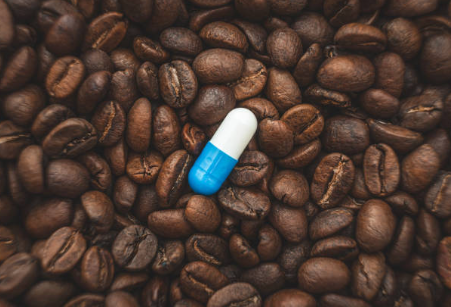 커피 원두 위에 놓인 파란색과 흰색 캡슐 영양제, 커피와 영양제의 상관관계를 상징적으로 표현한 이미지