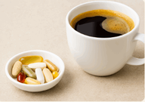 흰색 컵에 담긴 블랙 커피와 작은 접시에 담긴 다양한 알약 형태의 영양제가 함께 놓여 있는 모습, 커피와 영양제의 궁합을 상징적으로 표현